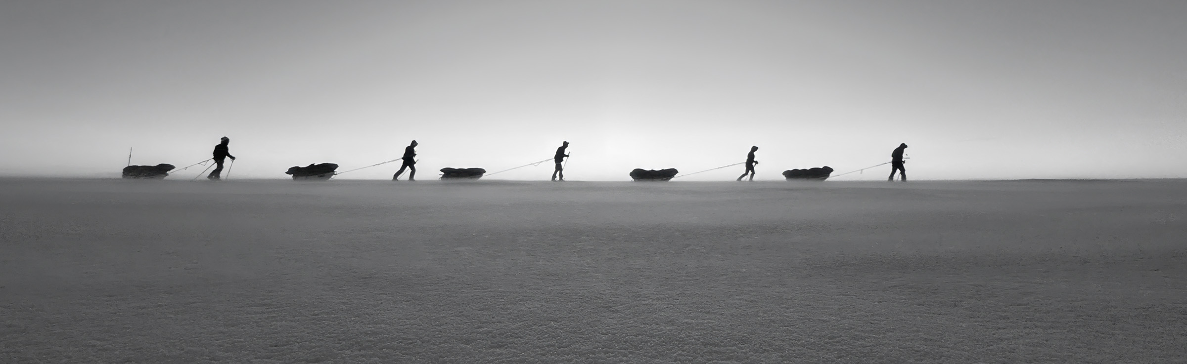 A team hauling sleds in a line across the ice.